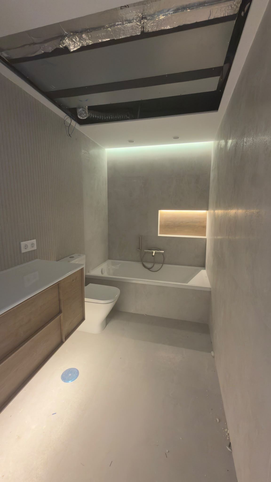 Baño con falso techo de pladur, línea de luz sobre la bañera y hornacina iluminada en la pared